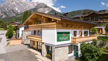 Charmantes Alpenhaus mit traditioneller Holzfassade und beeindruckendem Bergblick unter blauem Himmel.