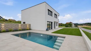 Modernes weißes Haus mit privatem Swimmingpool, gepflegtem Rasen und Steinmauer im Grünen.