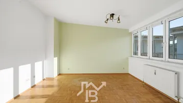 Helles Zimmer mit Parkettboden, hellgrüner Akzentwand und großen Fenstern, die viel Licht hereinlassen.