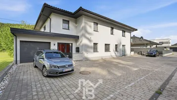 Modernes Einfamilienhaus mit gepflasterter Auffahrt, integrierter Garage und grüner Umgebung.
