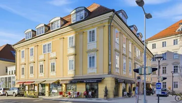 Historisches Gebäude mit gelber Fassade und Geschäften im Erdgeschoss an einer belebten Straßenecke.