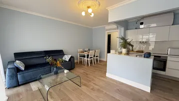 Heller Wohn-Essbereich mit offener Küche, Parkettboden und modernem Sofa in Blautönen.