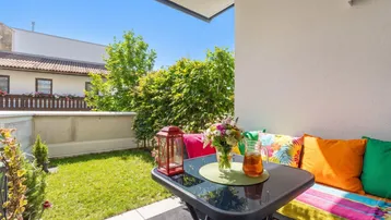 Sonnige Terrasse mit bunten Sitzgelegenheiten und kleinem Gartenbereich, umgeben von grünen Hecken.