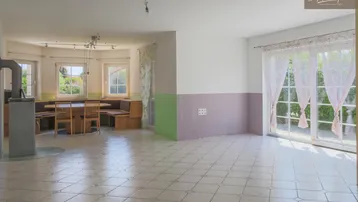 Geräumiger Wohn-Essbereich mit Fliesenboden, Kaminofen und Zugang zur Terrasse oder Garten.