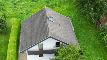 Luftaufnahme eines Einfamilienhauses mit Satteldach und gepflegtem Gartenbereich in grüner Umgebung.