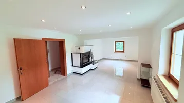 Helles Wohnzimmer mit modernem Kaminofen, Fliesenboden und Blick ins Grüne.