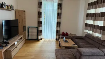 Gemütliches Wohnzimmer mit großem Sofa, Holzboden und Fenster mit Vorhängen.