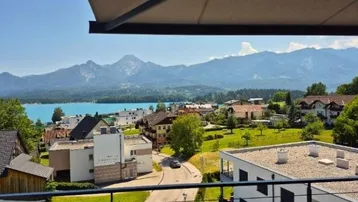 Panoramablick von einem Balkon auf einen türkisfarbenen See und die umliegende Berglandschaft.