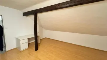 Heller Raum im Dachgeschoss mit Holzbalken, Schreibtisch und Laminatboden.