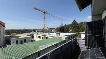 Balkon mit Solarmodulen und weitem Blick über die Stadt und eine Baustelle.