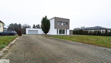 Moderne weiße Villa mit Holzfassadenelementen und großzügiger gepflasterter Auffahrt.