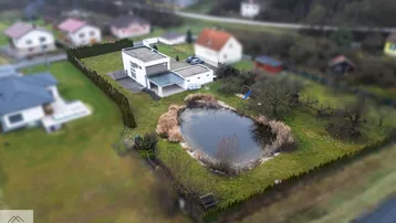 Luftaufnahme des modernen Hauses mit großem Garten, Teich und umliegender Landschaft.