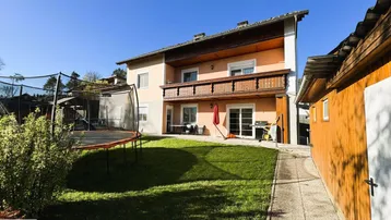 Großer Garten mit Rasenfläche, Trampolin und Zugang zu einer Terrasse am Haus.