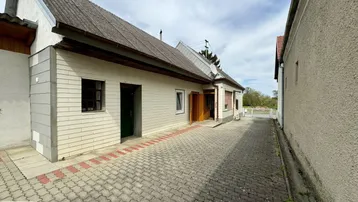 Ansicht des Hauses von der Seite mit gepflasterter Zufahrt und Eingangsbereich unter bewölktem Himmel.