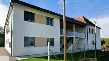 Modernes Mehrfamilienhaus mit weißer Fassade, Rollläden und einem kleinen Balkonbereich.