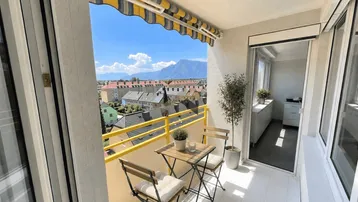 Heller Balkon mit Markise, Sitzgelegenheiten und weitem Blick auf die umliegende Berglandschaft.