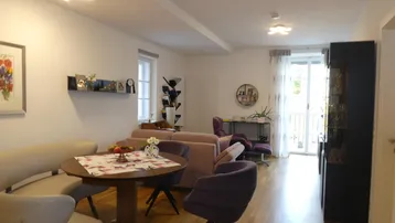 Heller offener Wohn-Essbereich mit Holzboden, gemütlicher Sitzecke und Zugang zum Balkon.