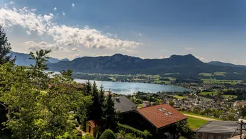 Panoramablick auf den Mondsee und die umliegende Berglandschaft unter blauem Himmel.