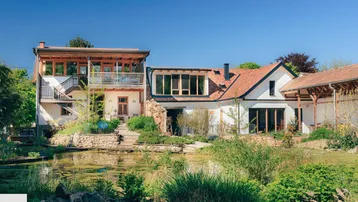 Großzügiges Anwesen mit Teich, umgeben von viel Grün und einer charmanten Architektur.