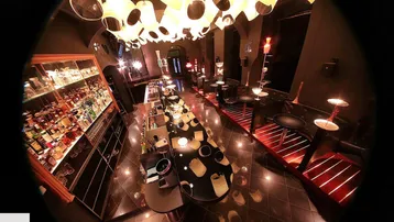 Innenansicht einer Bar mit einzigartiger Deckenbeleuchtung, dunklen Fliesen und einer gut bestückten Bar.