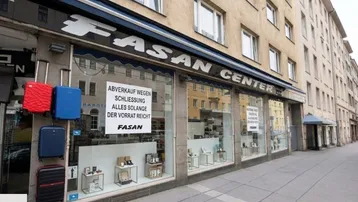 Straßenansicht eines Gebäudes mit einem Geschäft im Erdgeschoss, das Koffer ausstellt und einen Räumungsverkauf ankündigt.