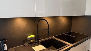 Moderne Küche mit weiß-glänzenden Schränken, dunkler Arbeitsplatte und integriertem Induktionskochfeld.