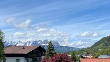 Panoramablick auf die majestätischen Berge und die umliegende grüne Landschaft unter blauem Himmel.