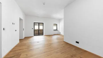 Helles Zimmer mit Holzboden und Zugang zu einem Balkon, ideal als Wohn- oder Schlafbereich.