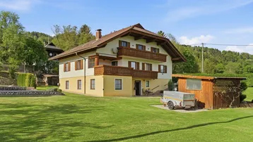 Traditionelles Haus mit großem Garten und Holzbalkonen unter blauem Himmel.