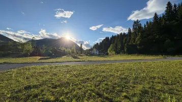 Weitläufige Landschaft mit Bergen, Wald und einem sonnigen Feld im Vordergrund bei Sonnenuntergang.