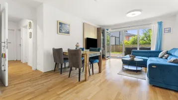 Helles Wohn- und Esszimmer mit Holzboden, blauer Couch und Zugang zur Terrasse.