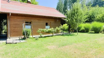 Rustikales Holzhaus mit rotem Dach und weitläufigem Gartenbereich unter blauem Himmel.