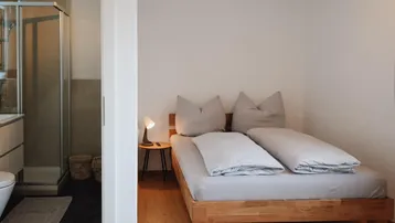 Schlafzimmer mit Holzbett und angrenzendem Badezimmer mit Duschkabine.