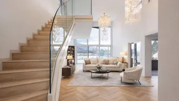 Großzügiges Wohnzimmer mit eleganter Treppe, hohen Decken, großen Fenstern und luxuriösen Kronleuchtern.