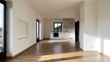 Heller, leerer Raum mit Laminatboden und integrierter Küchenzeile, durchflutet von Sonnenlicht.