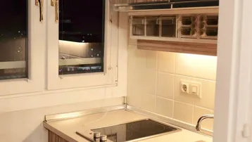 Kompakte Küchenzeile mit Holzdekorfronten, integriertem Kochfeld und Blick auf die Stadt bei Nacht.