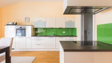 Moderne Küche mit weißen Hochglanzfronten, grüner Rückwand und Kochinsel mit Induktionskochfeld.