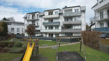 Mehrfamilienhaus mit Balkonen und einem gemeinschaftlichen Spielplatz im Vordergrund.