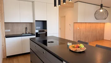 Moderne Küche mit weißen Schränken, dunkler Kücheninsel und Holzakzenten, offen zum Wohnbereich.
