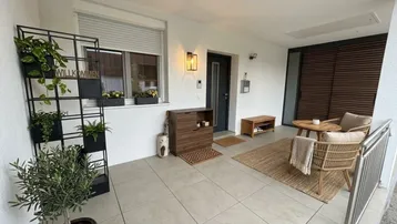 Überdachte Terrasse mit Sitzgelegenheiten, Pflanzen und Blick ins Grüne.
