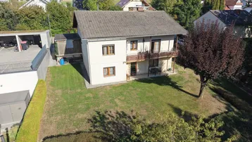Luftaufnahme eines Einfamilienhauses mit großem Garten, Carport und umliegender Wohnbebauung.
