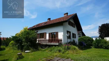 Freistehendes Einfamilienhaus mit Satteldach, Balkon und umgebendem Garten unter blauem Himmel.