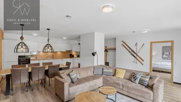 Helles, offenes Wohnzimmer mit integrierter Küche und Essbereich, modern eingerichtet mit Holzboden.