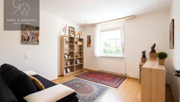 Gemütliches Wohnzimmer mit Holzboden, Teppichen, Sofa und Bücherregal, hell durch Fenster.