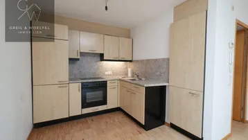 Funktionale Küche mit hellen Holzschränken, integriertem Backofen und Parkettboden.