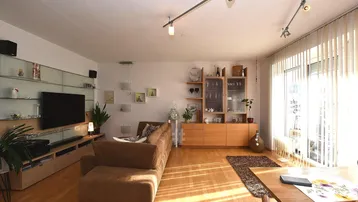 Helles Wohn- und Esszimmer mit Parkettboden, großen Fenstern und moderner Einrichtung.