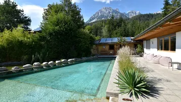 Großer Außenpool mit gepflasterter Terrasse und Bergblick im Hintergrund.