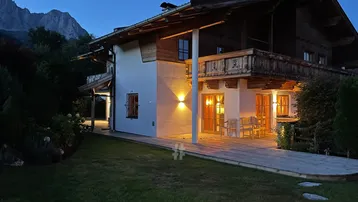 Charmantes Chalet bei Nacht mit beleuchteter Terrasse und Bergblick im Hintergrund.