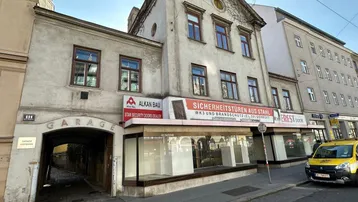 Altes Gebäude mit Ladenlokalen im Erdgeschoss und einer Garageneinfahrt an der Seite.