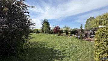 Großer, gepflegter Garten mit Rasenfläche, Bäumen und einer kleinen Terrasse im Hintergrund.